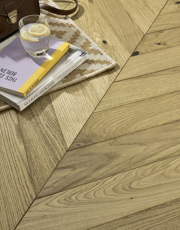 Close-up of chevron wood floor with books and a glass.
